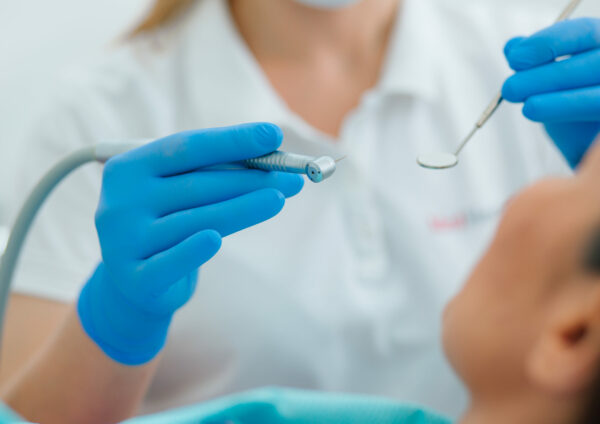 Close up of a dentist in blue rubber gloves holding medical instruments near the face of a patient